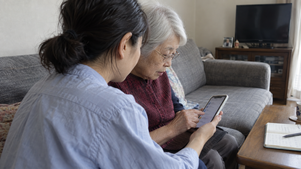 高齢の親と家族が居間でスマートフォンの通知と連絡方法を確認する様子